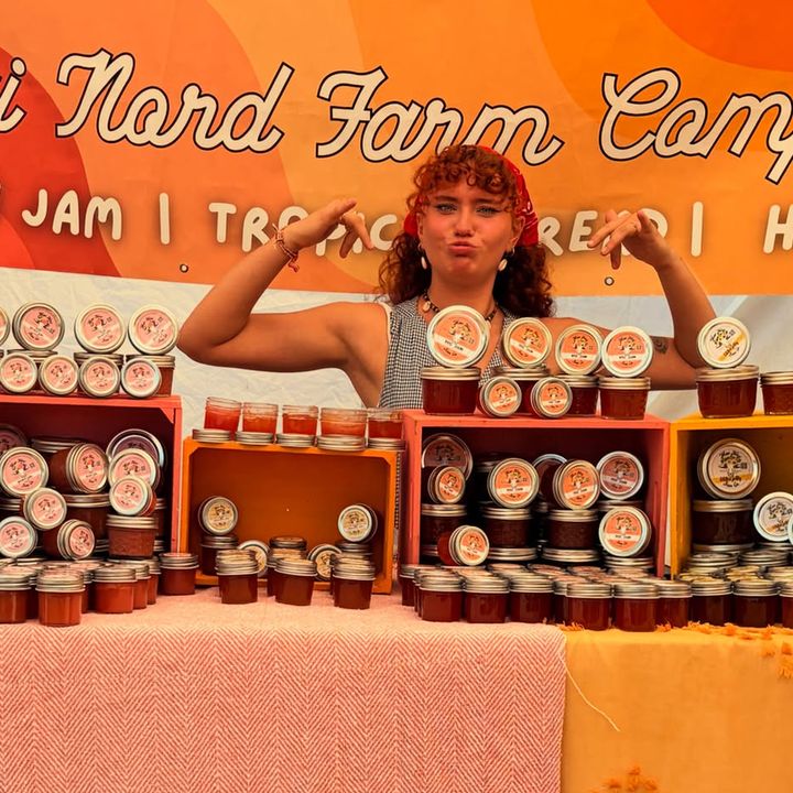 A woman in a red bandana at the booth under the Maui Nord Farm Company banner, jars stacked in front of her