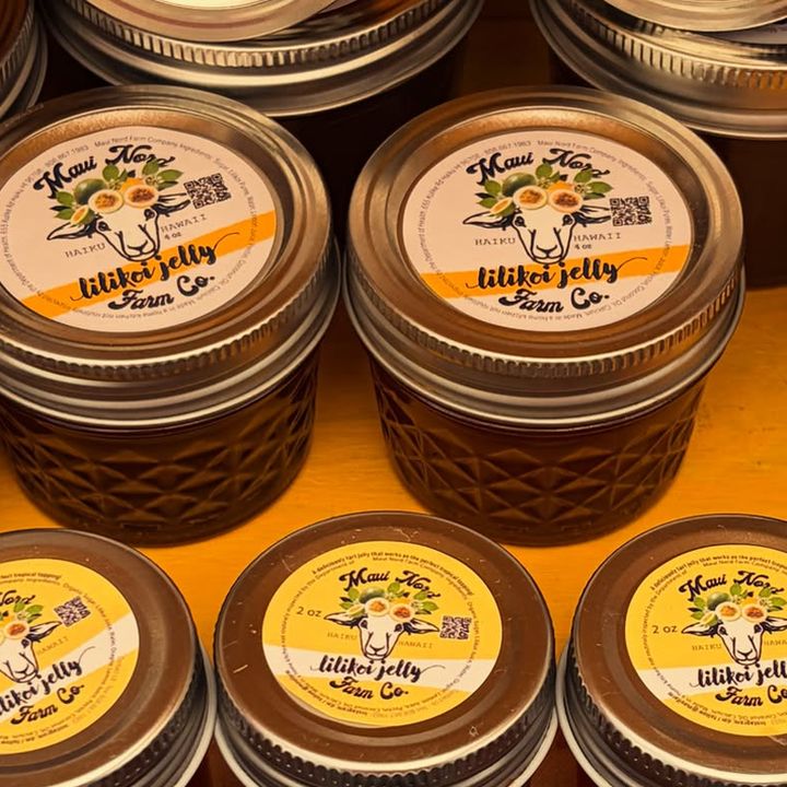 Jars of lilikoi jelly in rows on a shelf, yellow lids printed with the sheep mark