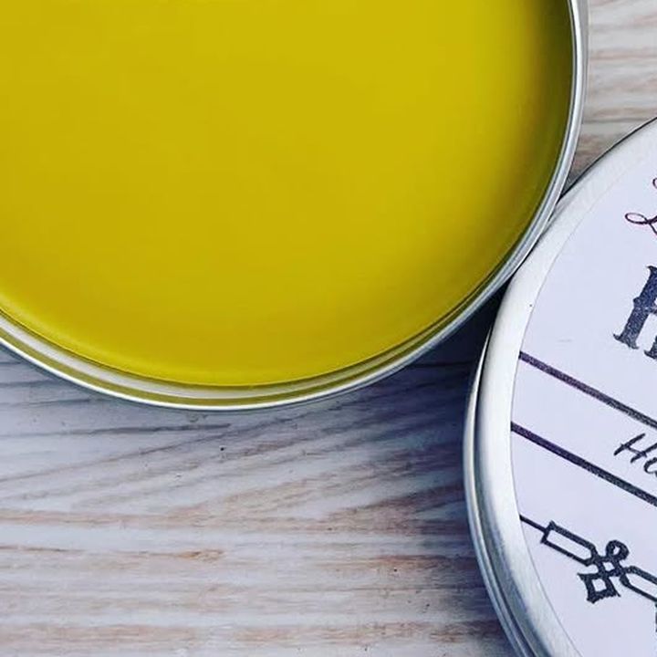 An open tin of beeswax hand salve on a whitewashed board