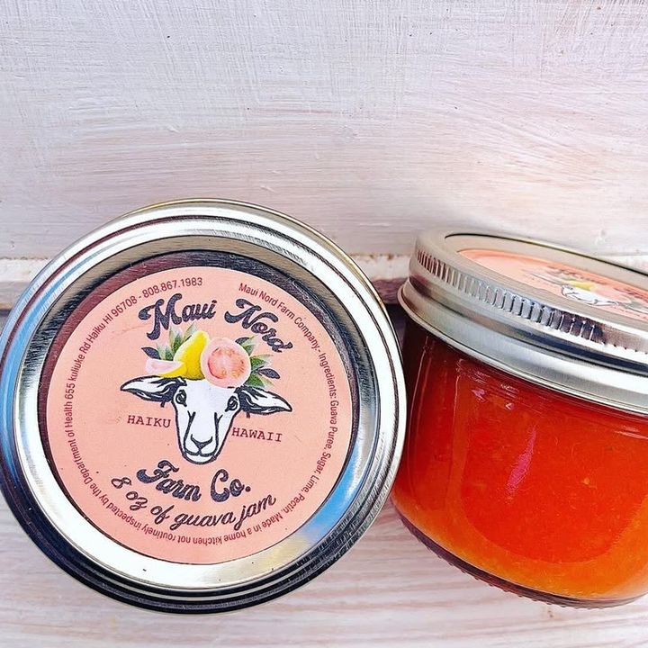 Two jars of guava jam on a whitewashed board, one open to show the jam
