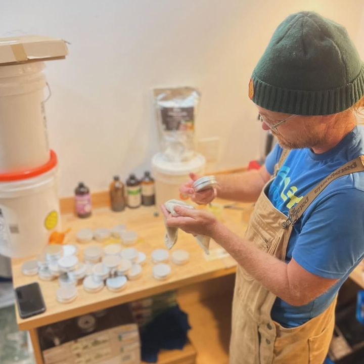 A man in a beanie and overalls sorting jar lids at a workbench